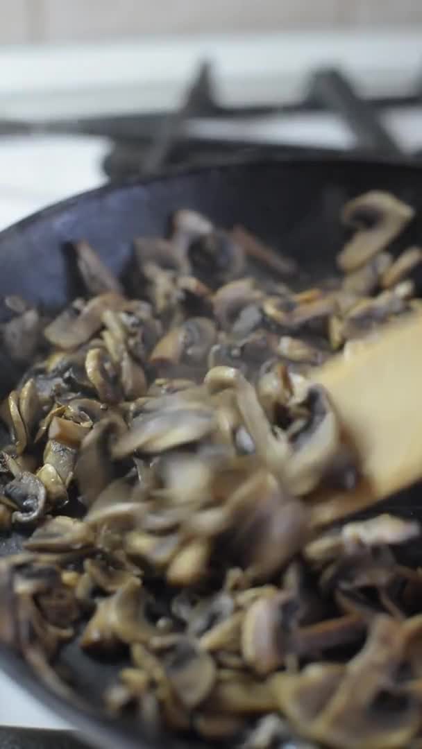 在一个炽热的黑色煎锅里 垂直的视频油炸香菇翻炒 用木勺搅拌半熟的炸蘑菇 — 图库视频影像
