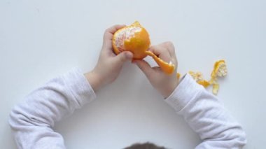 Çocuğun elleri mandalinayı soyar, yakın plan fotoğraf, yatay. Fikir, çocuklar için sağlıklı bir vitamin diyeti, iyi motor beceriler ve konuşma becerileri geliştirmek..