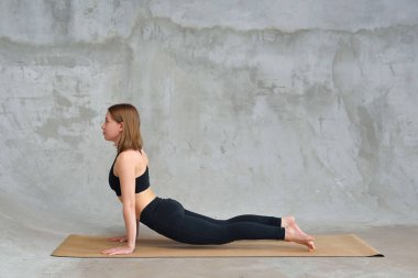 Güzel bir kadın Kobra pozu veriyor, Bhujangasana egzersizi yapıyor, yoga yapıyor, siyah spor giyinen çekici bir kız evde ya da yoga stüdyosunda spor yapıyor.