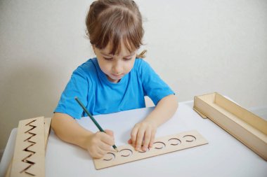 Anaokulunun ellerini yazıya hazırlamak için şablon yerleştirin. Erken gelişim kavramı. Kız yazmayı öğreniyor.
