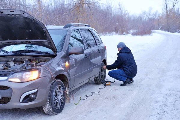 Man checking air pressure and filling air in the tires with Car eletric pump on road in winter on a snowy path in the forest using a pump. Broken cars concept.