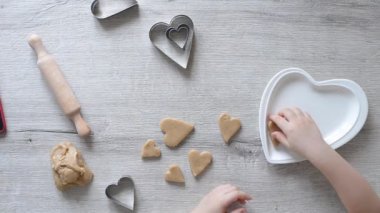 Bebek kalemleri, ebeveynler için Sevgililer Günü 'nde çocuklar için zencefilli kurabiye yapmak için rendelenmiş kurabiyelerin üzerine çiğ kurabiye serer. Çocuklar için yemek pişirme eğitimi. İnce motor becerilerin erken çocuk gelişimi
