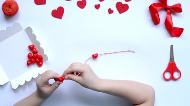 Sevgililer günü bilekliği için bebek kalemleri kırmızı boncuk kalpler dizer. El yapımı bebek dekorasyonu. El işi konsepti. Adım 3. Düzen, üst görünüm