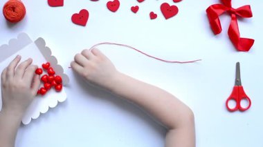 Sevgililer günü bilekliği için bebek kalemleri kırmızı boncuk kalpler dizer. El yapımı bebek dekorasyonu. El işi konsepti. Adım 3.Düzen, üst görünüm.