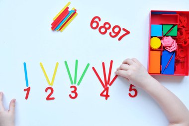 Çocuk sayı doğrusunu ve geometrik şekilleri öğreniyor. Anaokulu öğrencisi Montessori malzemeleriyle çalışıyor. Çocuklar için eğitici mantık oyuncakları. Çocukların elleri, yakın plan. Çocuk Gelişimi için Montessori Oyunları.