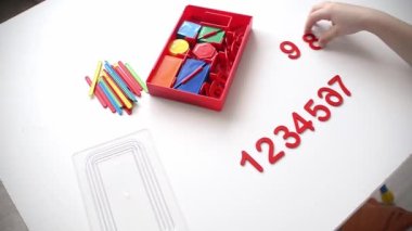 Çocuk sayı doğrusunu ve geometrik şekilleri öğreniyor. Anaokulu öğrencisi Montessori malzemeleriyle çalışıyor. Çocuklar için eğitici mantık oyuncakları. Çocukların elleri, yakın plan. Çocuk Gelişimi için Montessori Oyunları.