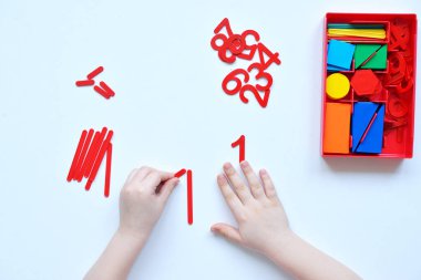 Çocuk sayı doğrusunu ve geometrik şekilleri öğreniyor. Anaokulu öğrencisi Montessori malzemeleriyle çalışıyor. Çocuklar için eğitici mantık oyuncakları. Çocukların elleri, yakın plan. Çocuk Gelişimi için Montessori Oyunları.