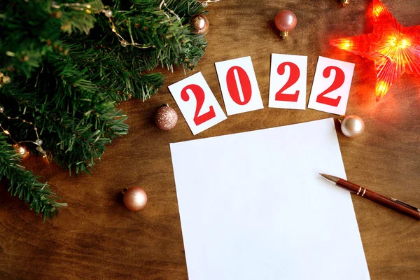 wish list on a wooden background with the numbers 2021, a blank sheet of paper and a pen for writing wishes, led is a garland, a red star for the Christmas tree. Christmas composition.