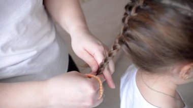 Anne kadın, kızının saç stilini evde beyaz bir kıza yapıyor. Kendine özen gösterme konsepti. Saçları örüyor..