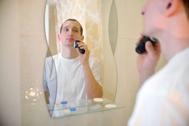 Beyaz tişörtlü bir adam aynanın önündeki banyoya elektrikli jilet attı. Kişisel Hijyen Konsepti