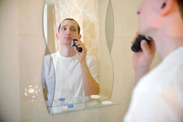 Beyaz tişörtlü bir adam aynanın önündeki banyoya elektrikli jilet attı. Kişisel Hijyen Konsepti