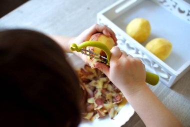 Pratik yaşam alanından ders almak için patatesleri montessori malzemesiyle soyan çocukların elleri. Soyucu, patates, tabak, tepsi. Evdeki yaşam tarzı