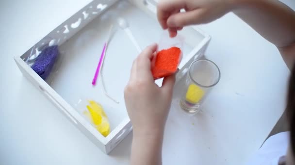 一个女的用勺子撒蜡 用细小的石蜡粒做成蜡烛 孩子们的钢笔躺在一张白色的桌子上 蒙台梭利材料剪刀 蜡烛杯 — 图库视频影像