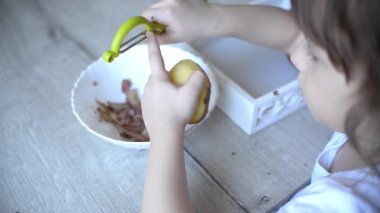 Pratik yaşam alanından ders almak için patatesleri montessori malzemesiyle soyan çocukların elleri. Soyucu, patates, tabak, tepsi. Evdeki yaşam tarzı