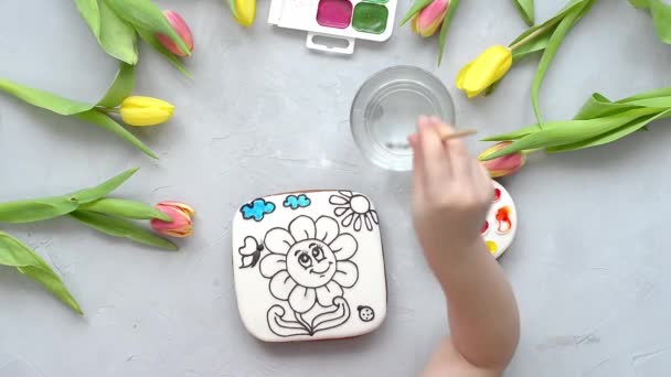 女の子が食べ物染料でジンジャーブレッドを描きます 子供のためのぬり絵は灰色のテーブルの上にある 子供へのオリジナル食用の贈り物という考え方です 優れた運動能力の開発 — ストック動画