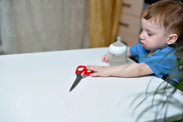 Danger in the home, sharp objects are dangerous for young children. little boy picks up scissors from the table and can hurt himself.