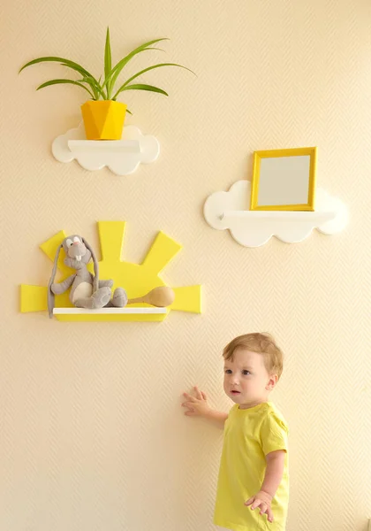 时尚而现代的室内设计 孩子房间的家 蹒跚学步的男孩从架子上拿起一只灰兔的软玩具 — 图库照片
