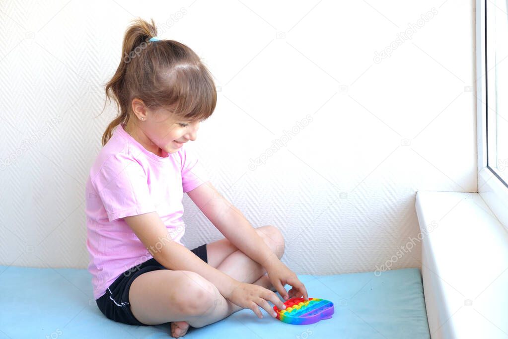 a girl in a pink t-shirt plays with a trendy toy pop it. colorful antistress sensory toy fidget push pop it in kid's hands, can be used for training with autistic people