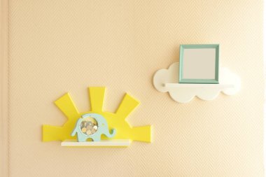 Şık ve modern iç tasarım. Çocuk odası için geldim. Çocukların rafları bej bir duvarda beyaz bulutlar şeklinde, üzerinde bozuk paralar ve fotoğraf çerçevesi olan mavi bir kumbara var.