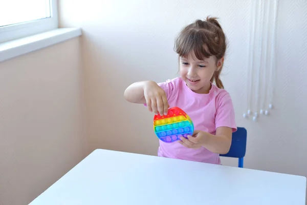 一个穿着粉色T恤的女孩玩一个时髦的玩具弹奏它 五彩缤纷的减压玩具小提琴手把它弹出在孩子的手上 可用于自闭症患者的训练 免版税图库照片