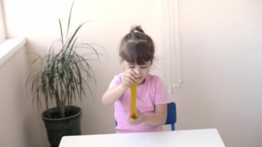 Bir kızın sarıya sarılıp beyaz bir masada altın renkli sümüksü sümükle gerildiği yakın plan. Çocuk balçık oyuncağıyla oynuyor. Sümük yapıyorum. Uzayı kopyala Diy konsepti. Deney bilimsel yöntemi zamanı..