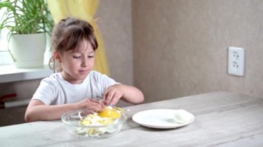 Anaokulu öğrencisi kız çocuk mutfakta yemek pişiriyor. Hurda malzemelerle günlük hayatta iyi motor becerilerin geliştirilmesi. Çocuk yumurtaları sarı bir yumurta kesiciyle kesiyor..
