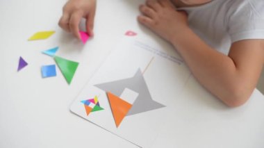 Masada oturan anaokulu öğrencisi bir kız geometrik bir figürden resim topluyor. Montessori 'nin erken çocukluk gelişimi kavramı. bir mantık ve hayal gücü oyunu.
