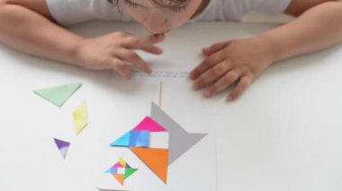 Masada oturan anaokulu öğrencisi bir kız geometrik bir figürden resim topluyor. Montessori 'nin erken çocukluk gelişimi kavramı. bir mantık ve hayal gücü oyunu.