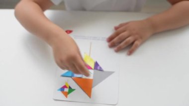 Masada oturan anaokulu öğrencisi bir kız geometrik bir figürden resim topluyor. Montessori 'nin erken çocukluk gelişimi kavramı. bir mantık ve hayal gücü oyunu.