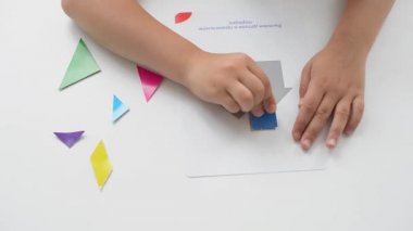 Masada oturan anaokulu öğrencisi bir kız geometrik bir figürden resim topluyor. Montessori 'nin erken çocukluk gelişimi kavramı. bir mantık ve hayal gücü oyunu.