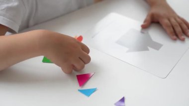 Masada oturan anaokulu öğrencisi bir kız geometrik bir figürden resim topluyor. Montessori 'nin erken çocukluk gelişimi kavramı. bir mantık ve hayal gücü oyunu.