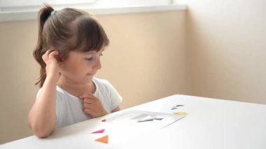 Masada oturan anaokulu öğrencisi bir kız geometrik bir figürden resim topluyor. Montessori 'nin erken çocukluk gelişimi kavramı. bir mantık ve hayal gücü oyunu.