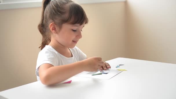 テーブルに座っている未就学児の少女は 幾何学的図形から図面を収集します モンテッソーリによる幼児期の発達の概念です 論理と想像力のゲームです — ストック動画