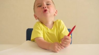 Küçük çocuk beyaz bir masada oturan kırmızı bir kalemle bir kağıt parçasına resim çizer. Eğitici oyun Montessori güzel motor becerileri. Erken gelişim kavramı