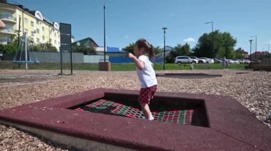 Kırmızı şortlu ve beyaz tişörtlü bir kız yaz sabahı bir çocuk parkında trambolinde zıplıyor. çocuklar dinlenme konsepti