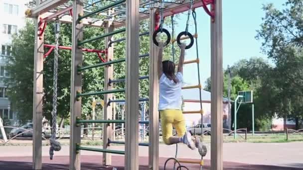 一个快乐的小女孩在公园里孩子们的操场上玩耍 这个孩子度假时在街上做体操圈儿 那孩子在模拟器上参加体育运动 — 图库视频影像