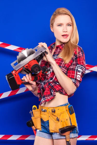 Costruttore ragazza su uno sfondo blu con uno strumento di costruzione professionale in un casco protettivo — Foto Stock