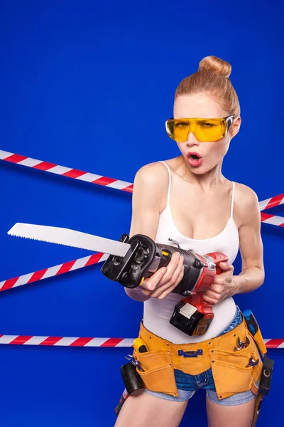 Builder girl on a blue background with a professional building tool in a protective helmet