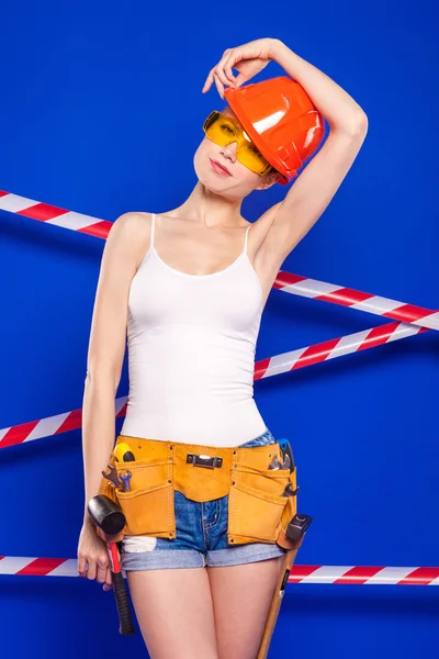 Construtor menina em um fundo azul com uma ferramenta de construção profissional em um capacete de proteção — Fotografia de Stock