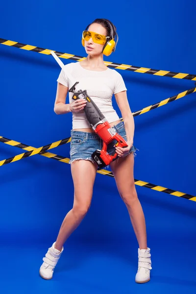 Seksowny brunetka konstruktora na niebieskim tle z elektrycznym narzędzie w rękach — Zdjęcie stockowe