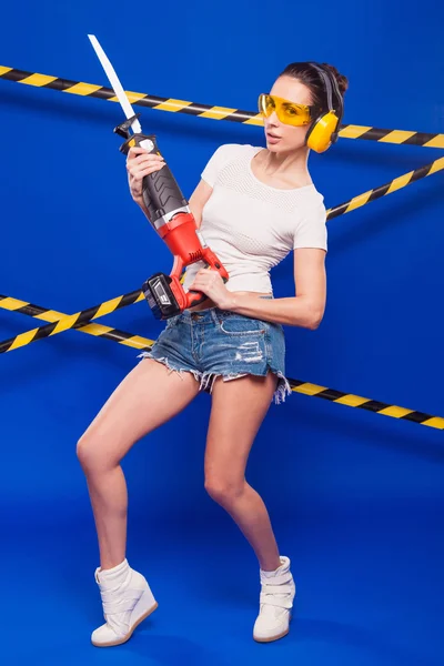 Seksowny brunetka konstruktora na niebieskim tle z elektrycznym narzędzie w rękach — Zdjęcie stockowe