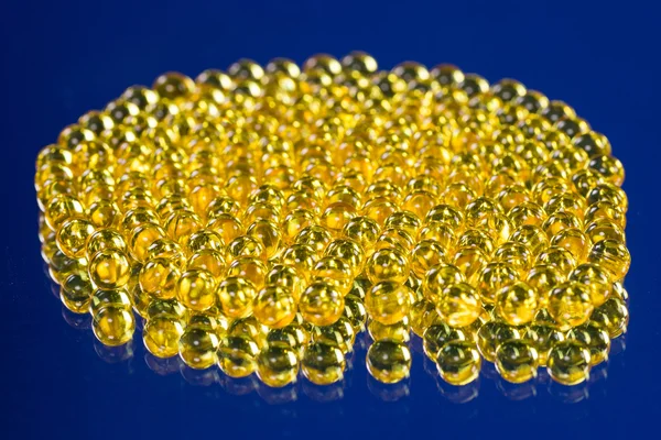 Cápsulas médicas amarillas en una superficie de espejo — Foto de Stock