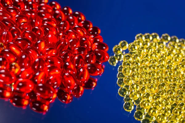 Cápsulas médicas amarillas y rojas en una superficie de espejo — Foto de Stock