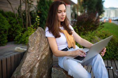 Çekici genç bir kadın öğle yemeği molasında bahçede dizüstü bilgisayarla oturuyor.