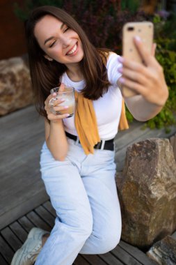 Genç kadın serbest çalışan parkta oturuyor ve elinde telefonla kahve molasından zevk alıyor.