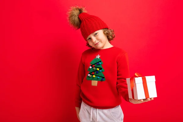 Bouclé blond garçon avec un cadeau dans ses mains sur un fond rouge — Photo