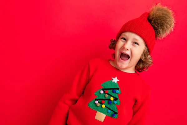 Chico fresco con rizos sobre un fondo rojo en un suéter con un árbol de Navidad — Foto de Stock