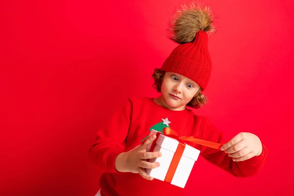 Lockigt blond pojke med en gåva i händerna på en röd bakgrund — Stockfoto