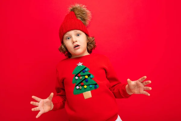 Cool garçon avec des boucles sur un fond rouge dans un pull avec un arbre de Noël — Photo