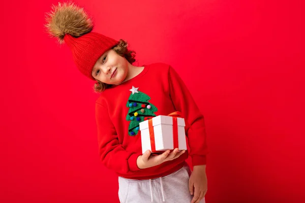 Kręcone blond chłopiec z prezentem w dłoniach na czerwonym tle — Zdjęcie stockowe